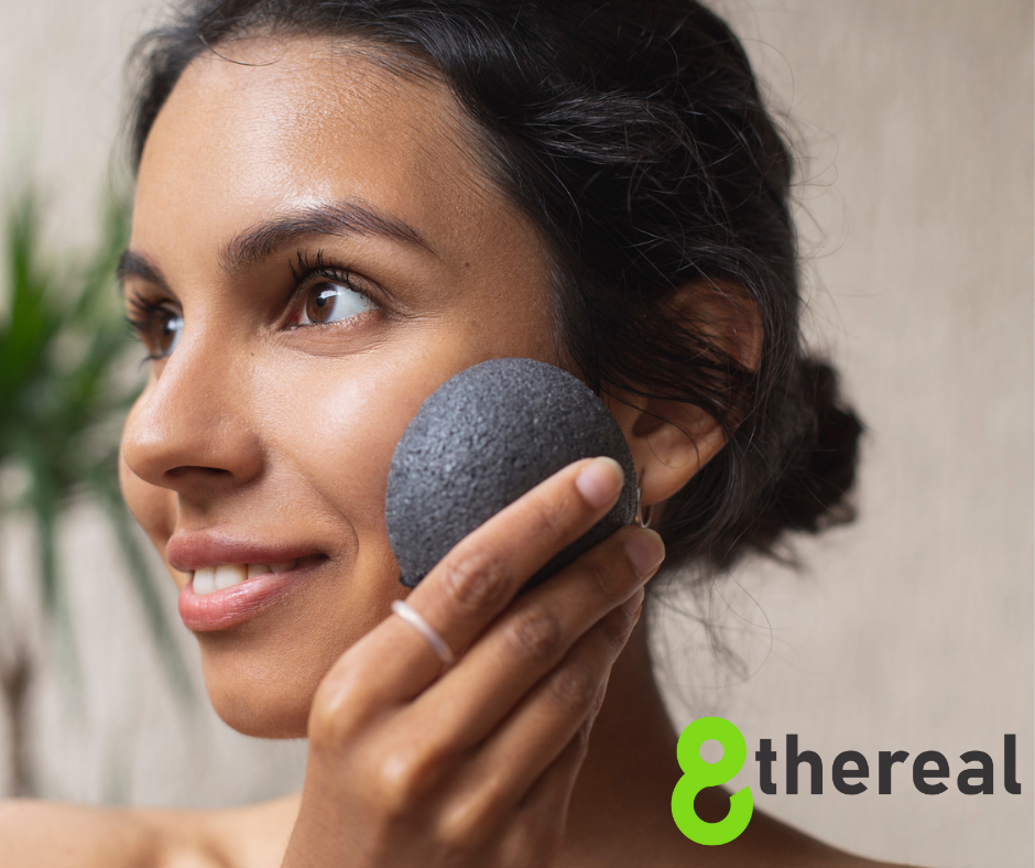 Konjac Sponge Face Treatment | Close up photo of woman using konjac sponge on her face. Her hair is in a bun as she stands in front of blurred background. 8thereal is spelled out on the bottom right corner | 8thereal